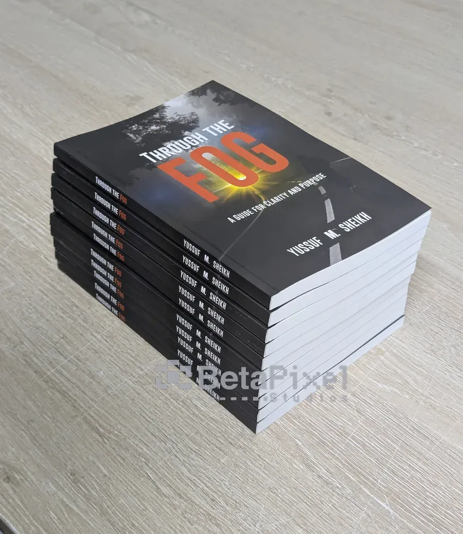Stack of printed paperback copies of the book Through the Fog with a red title on a dark cover