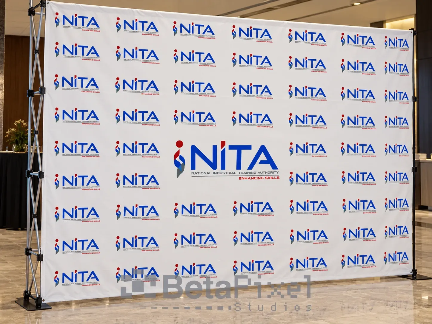 Media backdrop banner with a repeating training authority logo pattern on a portable pop-up frame at an indoor event