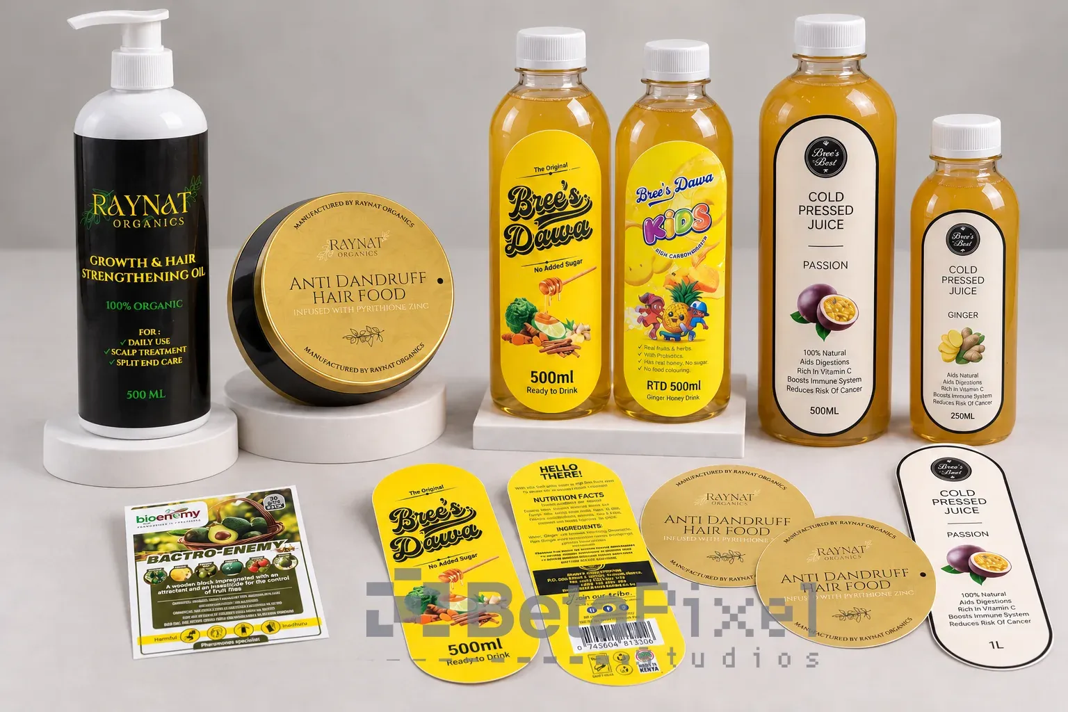Printed product labels on a hair-oil bottle, a hair-food jar, ginger-honey drinks and cold-pressed juice bottles, with loose die-cut labels in front
