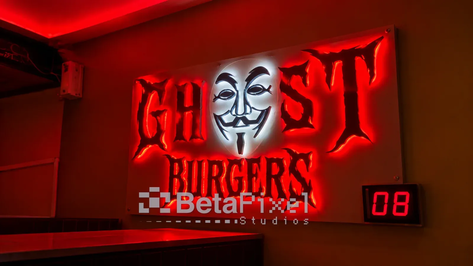 Illuminated restaurant wall sign with red-backlit 3D lettering and a glowing white mask logo above a dining table