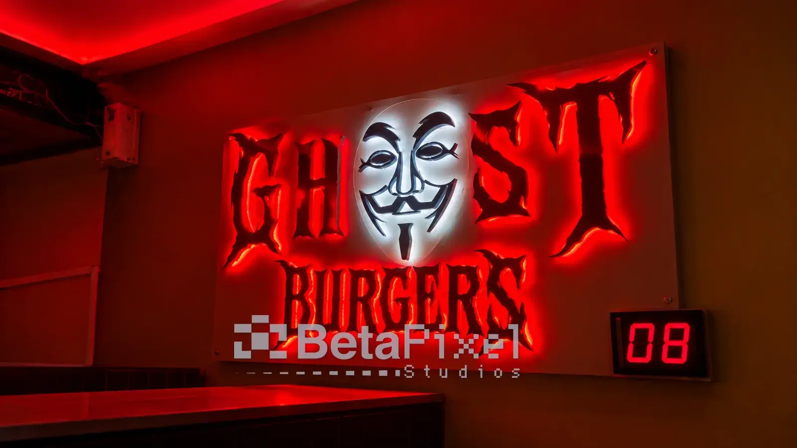 Illuminated restaurant wall sign with red-backlit 3D lettering and a glowing white mask logo above a dining table