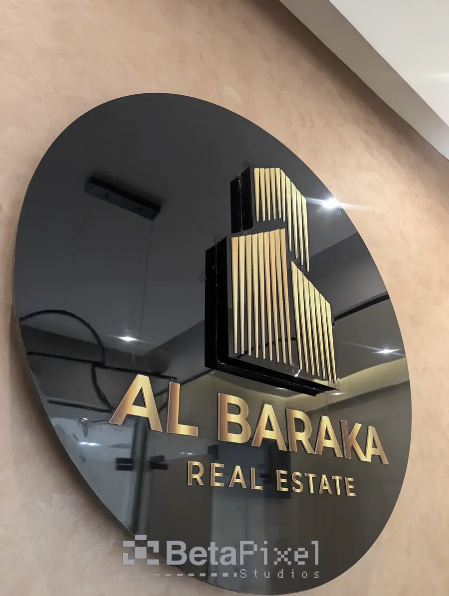 Black circular acrylic wall sign with a gold 3D building logo and lettering for a real estate company, installed in its office