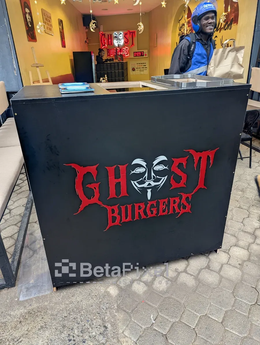 Black restaurant service counter wrapped with a red mask logo, with the illuminated wall sign behind