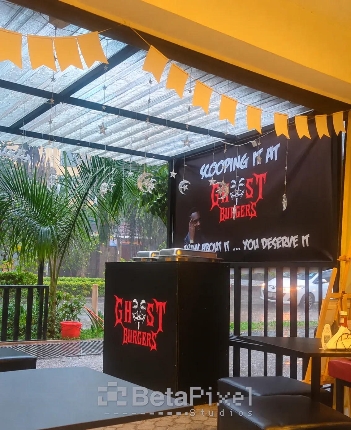 Restaurant interior with a large printed fabric banner, a branded service counter and bunting under a covered terrace