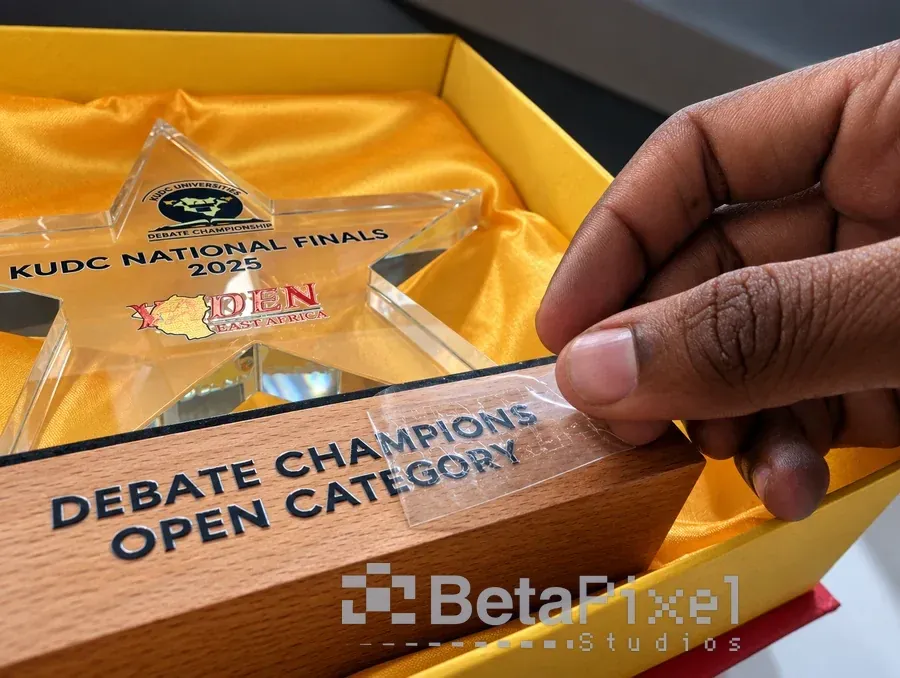 Hands pressing a UV DTF transfer onto the wooden base of an acrylic star award for a national debate championship
