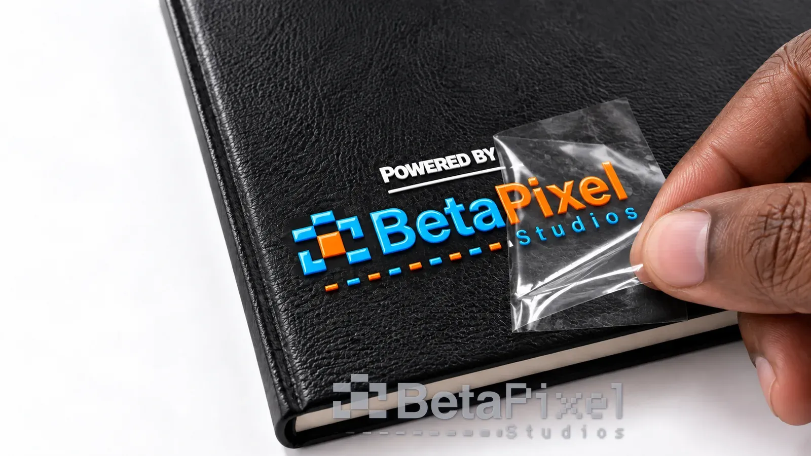 Hand peeling the clear film off a raised, glossy UV DTF logo on a black leather notebook