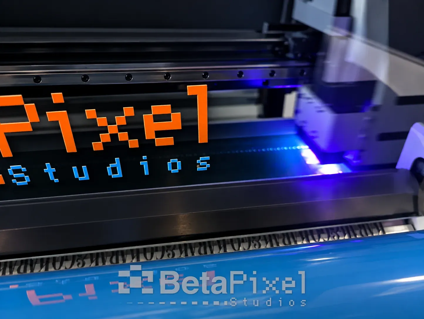 Betapixel Studios logo transfer coming off a UV DTF printer as the clear transfer film is laminated over the cured print